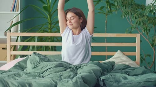 A Happy Young Woman Wakes Up in a Happy Mood Stretching Cheerfully in Bed