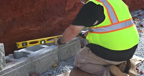 Trabalhando diligentemente, trabalhador da construção civil afixou bloco de concreto no muro de contenção