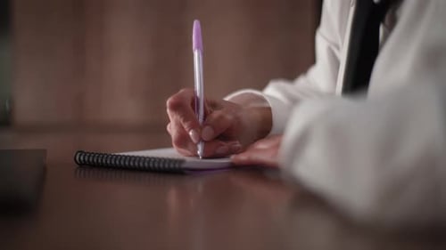 Person Writing in Notebook at Desk in Office
