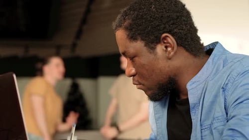 Homem negro escrevendo linhas de código em um PC de mesa com dois monitores e um laptop ao lado em um escritório elegante