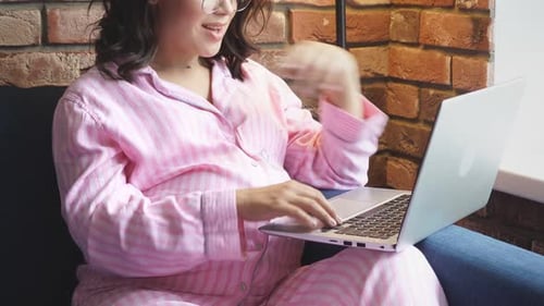 Pregnant Woman in Pajamas is Typing Something on Laptop at Home