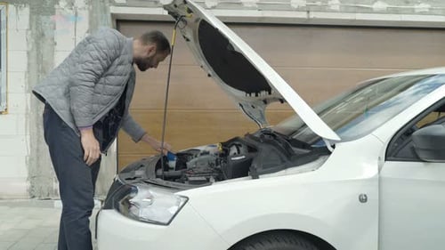 Young man diligently checking oil levels in his car on a sunny day at home
