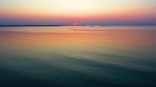 Start of Calm Ocean Sunrise with Dimmly Lit Sun over Small Islands on the Horizon. Waves Rippling wi
