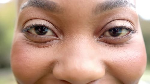 Portrait of close up of eyes of happy african american woman smiling in garden, in slow motion