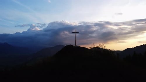 Aerial View of a Religious Christian Steel Cross on a Hill in the Mountainous Countryside in Sunset