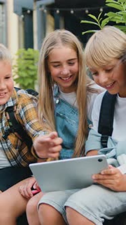 Happy Boys and Girls Together Use Tablet Device Smiling While Walking Sitting on Bench After School
