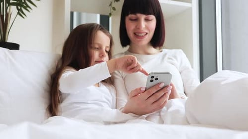 Mother and Child Watching Cell Phone in Bed