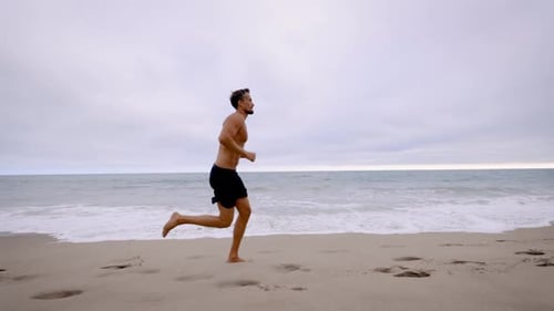 Hombre atlético corriendo en la playa del sur de California. Cámara lenta.
