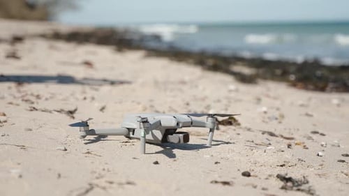 Drone Takeoff. Small portable grey drone flying up in the sky on a sand beach on a sunny day