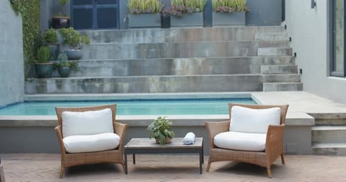 Camera is tilting up, pushing mats out; wicker chairs and table are staying centered revealing pool