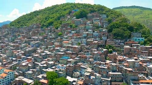 A Favela Community with Colorful Buildings Set Against Lush Green Hills Under a Clear Blue Sky in