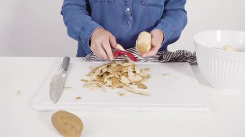 Step By Step Peeling Large Yellow Potatoes with a Vegetable Peeler on a White Wooden Board