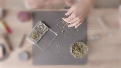 Blurred overhead shot: a man preparing a joint on a table with marijuana cannabis and tools, licking