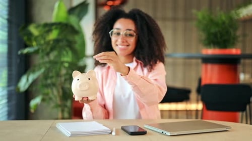 Fröhliche Frau spart Geld, indem sie lächelnd Münzen in ein Sparschwein einzahlt