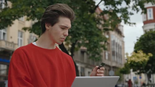 Young Man Using Laptop with Card in City