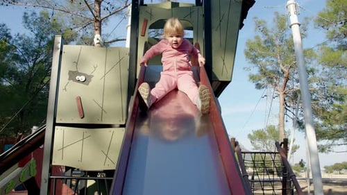 Cheerful Girl in Pink Tracksuit Slides Down Slide on Playground