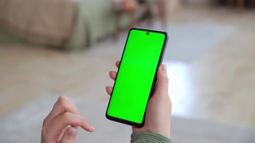 Back View of Young Woman Holding Smartphone with Green Screen for Copy Space Making Tap Swipes and