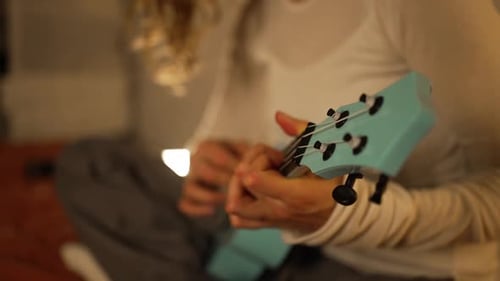 Person Playing Blue Ukulele Indoors at Home