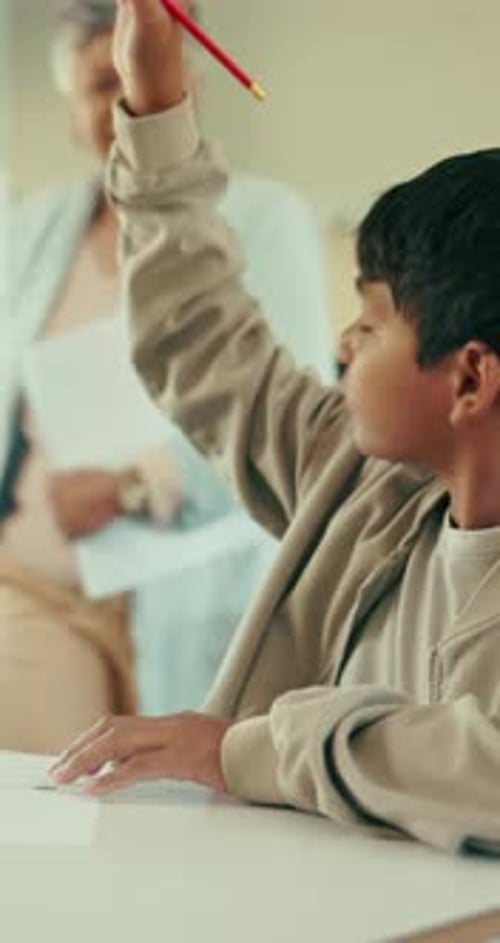 Boy Raises Hand as Teacher Assists in Classroom