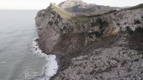 Rocky Cliff Washed By Wavy Endless Sea on Cloudy Day Cantabria Spain