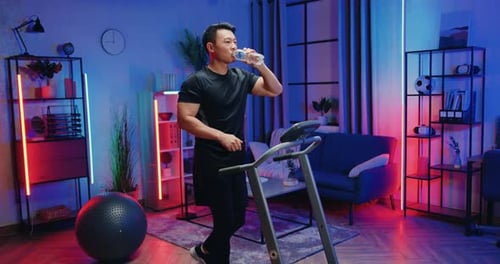 Man Drinking Water While Walking on a Treadmill