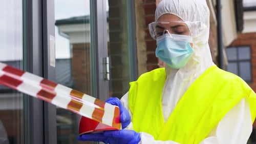 Healthcare worker enclosing building with caution tape during coronavirus pandemic