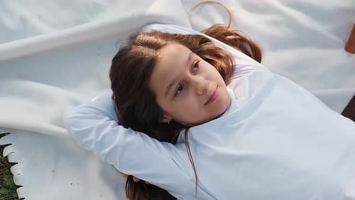 Aerial View Of Young Girl Lying Faced Up Thoughtfully On Blanket
