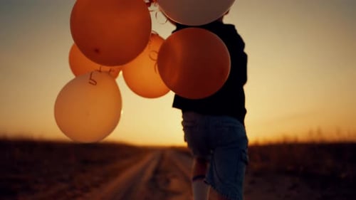 Celebrate Summer Holiday Little Boy with Balloons in Hands Running in Field Amazing Sunset or