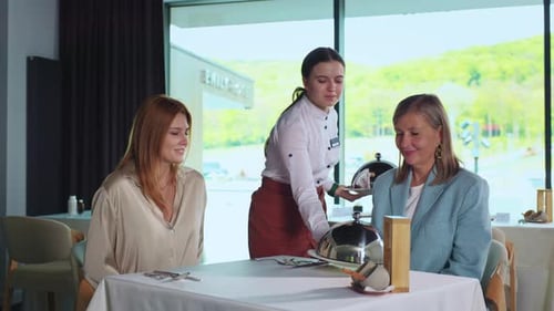 Two Elegant Women Sitting in Restaurant Friendly and Attentive Waitress Bringing Delicious Food to