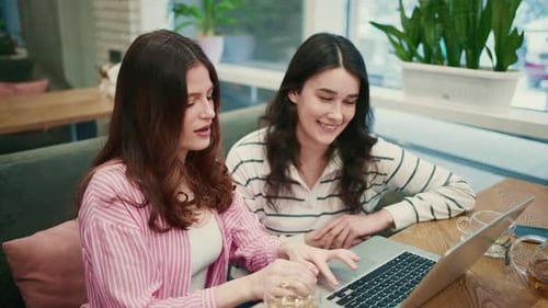Two Young Women Collaborating on a Laptop in a Cafe