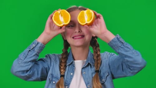 Closeup Cute Charming Girl Making Faces Showing Halves of Vitamin Orange Looking at Camera on Green
