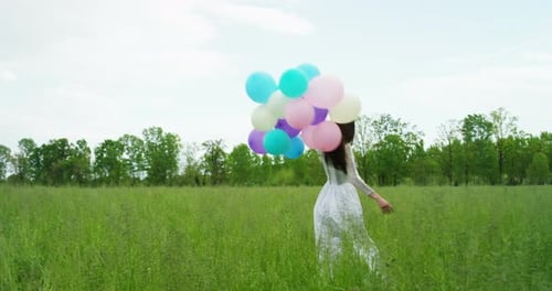 Woman Runs Through Field With Bunch of Balloons
