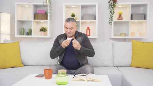 Man Blowing Nose with Tissue on Couch