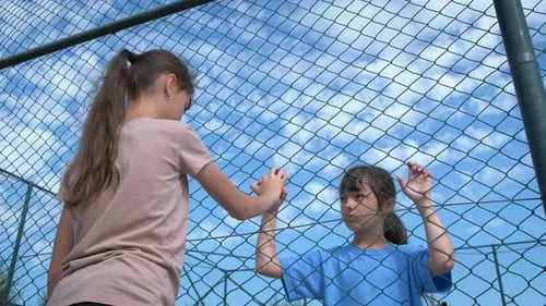 Girls Holding Hands Through a Chain Link Fence