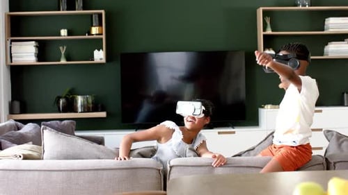 Happy african american brother and sister in vr headsets on sofa, copy space, slow motion