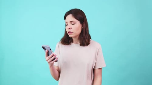 Frustrated Woman Using Smartphone on Teal Background