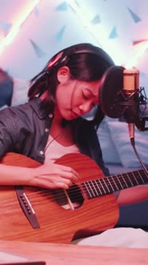 Asian Female Musician Playing Guitar and Singing in Home Recording Studio