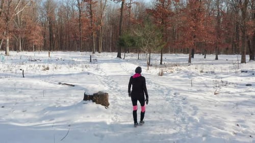 Woman walking alone on snowy winter forest path. Tracking shot from behind