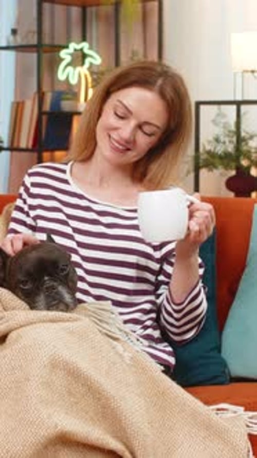 Woman Petting Dog on Sofa While Drinking Coffee