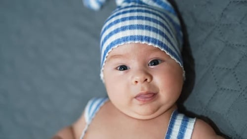 Cute toddler in adorable blue hat. Baby boy with plump cheeks at the grey backdrop.