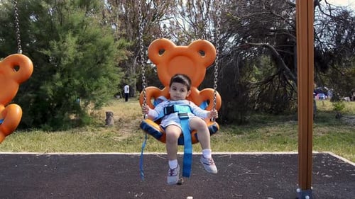 two years old boy relaxing on teddy bear shaped swing in the park