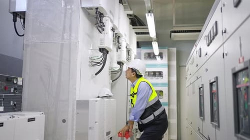 4K Asian man engineer working at factory server electric control panel room.