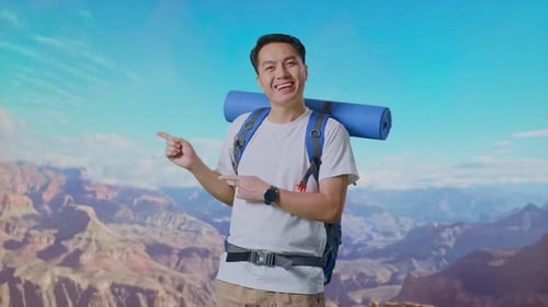 Asian Male Smiling And Pointing To Side At The Top of Mountain