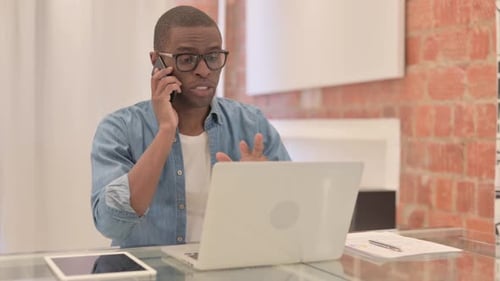 Man Talking on Phone at Desk with Laptop