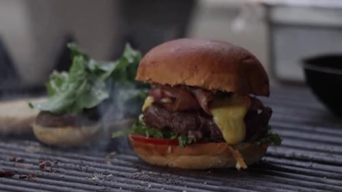 A Chef finishes cooking a meat hamburger with lettuce, tomato and melted cheese on the grill.