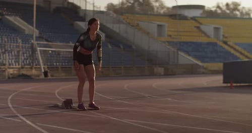 Young Female Sprinter Preparing for Run in Stadium