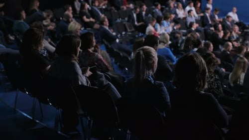 Audience seated in dark conference, watching presentation