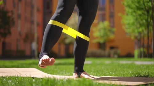 Closeup Unrecognizable Woman in Gym Pants Doing Leg Exercises with a Fitness Rubber Band Standing