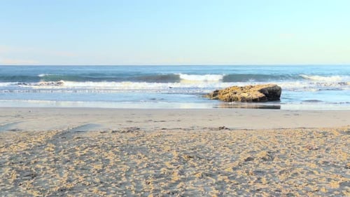Waves crashing on sandy beach with coastal rock