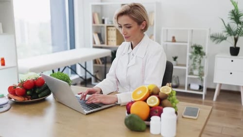 Woman at Desk Typing on Laptop Surrounded by Food
